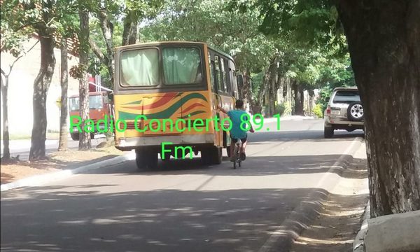 Adolescente en bicicleta se sostiene por la puerta de un colectivo en marcha